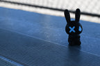 3D printed black monomoodz glow in the dark nixie bunny figure sitting outdoors on metal stadium bleachers by LayerPlay