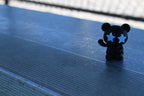 3D printed black monomoodz glow in the dark twinkle figure waving while sitting on metal stadium bleachers by LayerPlay