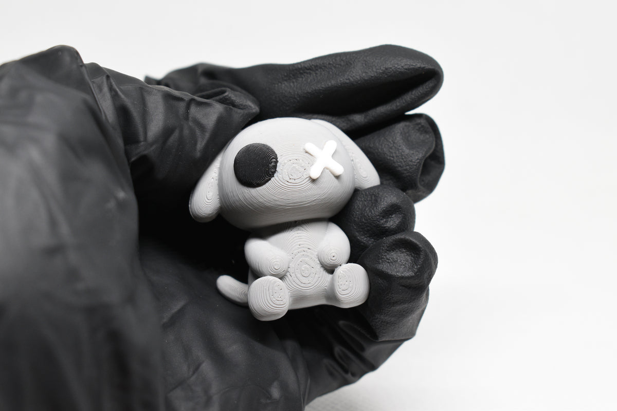 Hand in black glove holding cute 3D printed grey monomoodz glyphie dog desk figure close up by LayerPlay 