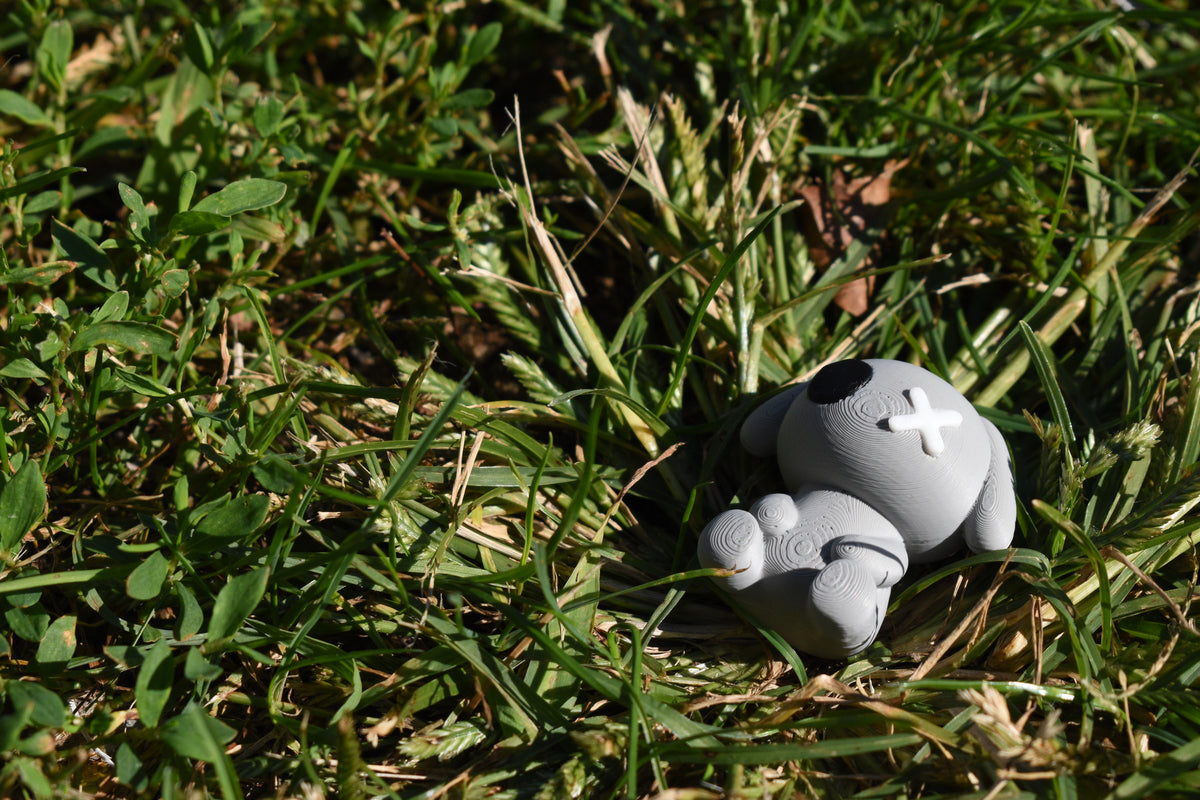 3D printed grey monomoodz glyphie dog desk figure reclining outdoors in green grass under sunlight by LayerPlay