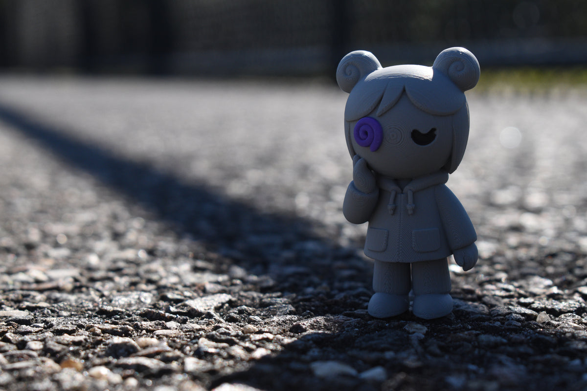 3D printed grey monomoodz kiri desk figure standing outdoors on asphalt pavement with dramatic lighting by LayerPlay