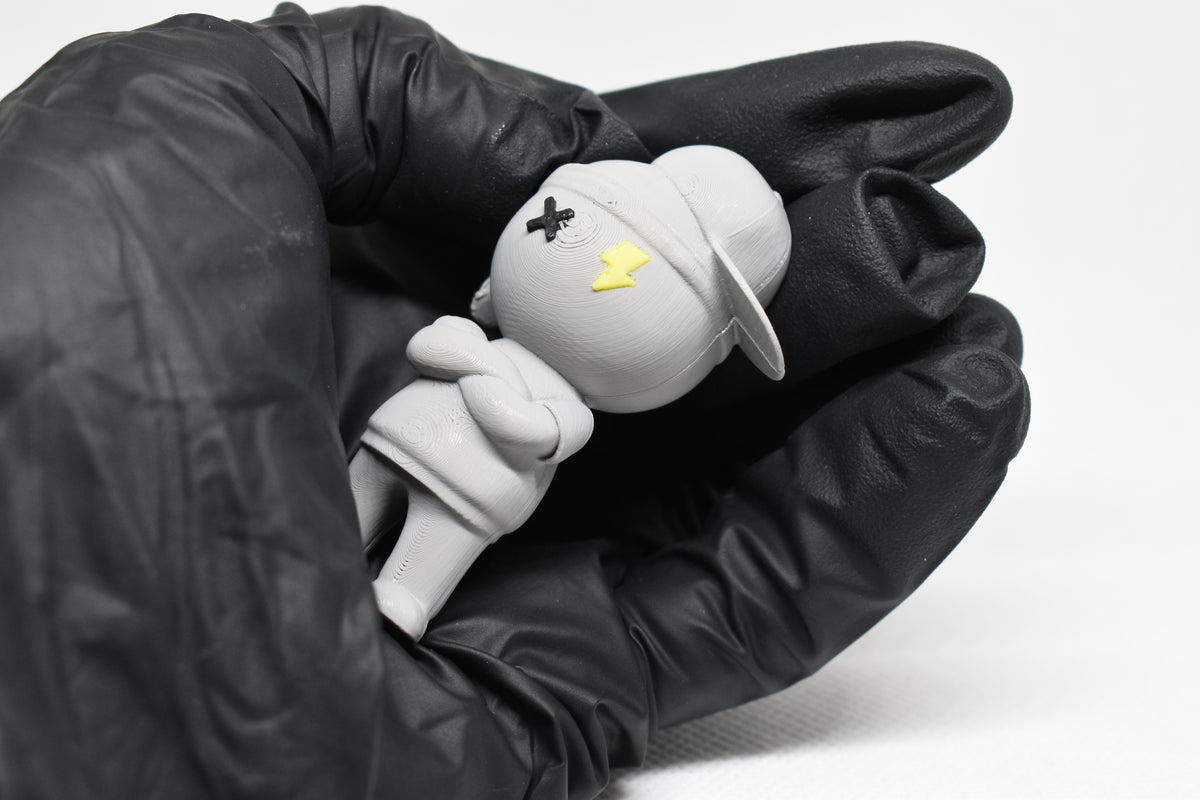 Hand in black glove holding cute grey 3D printed monomoodz lil static streetwear desk figure close up by LayerPlay