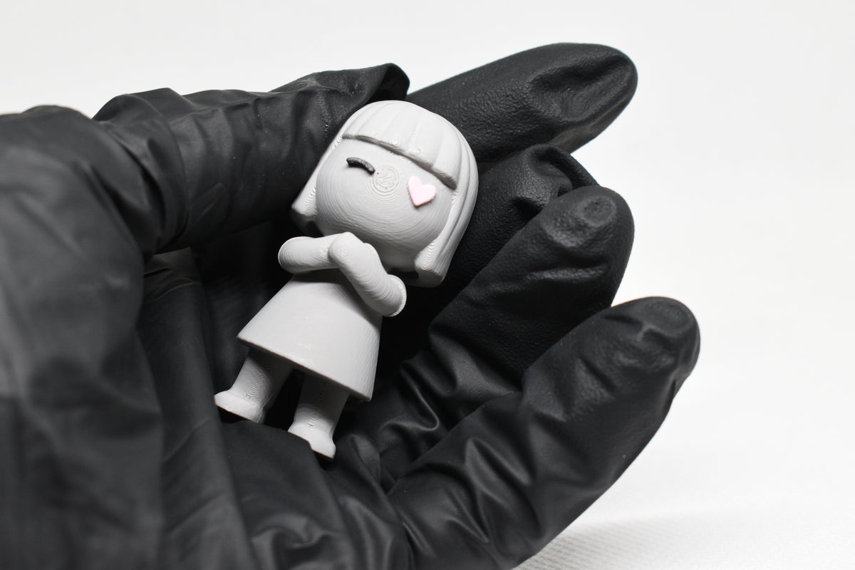 Hand in black glove holding cute grey 3D printed monomoodz luma girl desk figure close up by LayerPlay