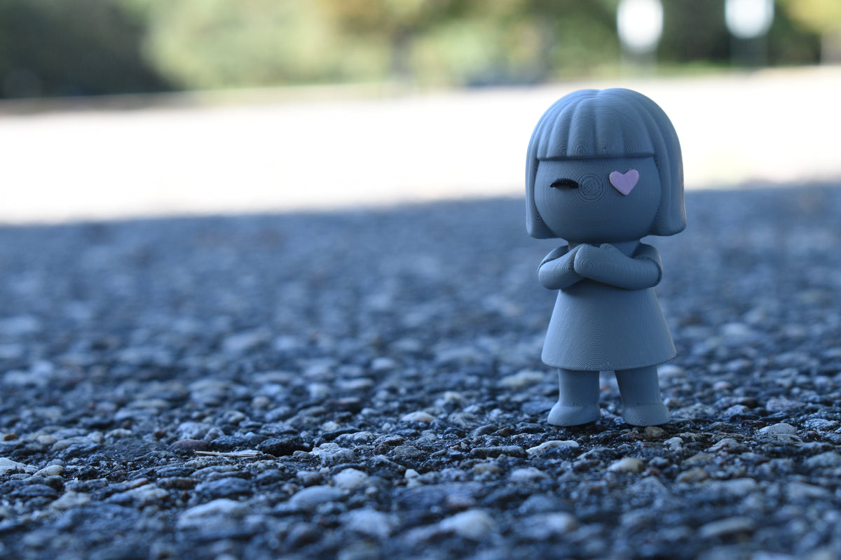 3D printed grey monomoodz luma desk figure standing outdoors on asphalt pavement with blurred background by LayerPlay