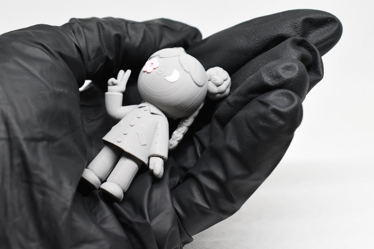Hand in black glove holding cute grey 3D printed monomoodz lunella desk figure close up by LayerPlay