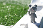 3D printed grey monomoodz lunella desk figure standing outdoors on a white ledge with a sunny green sports field background by LayerPlay