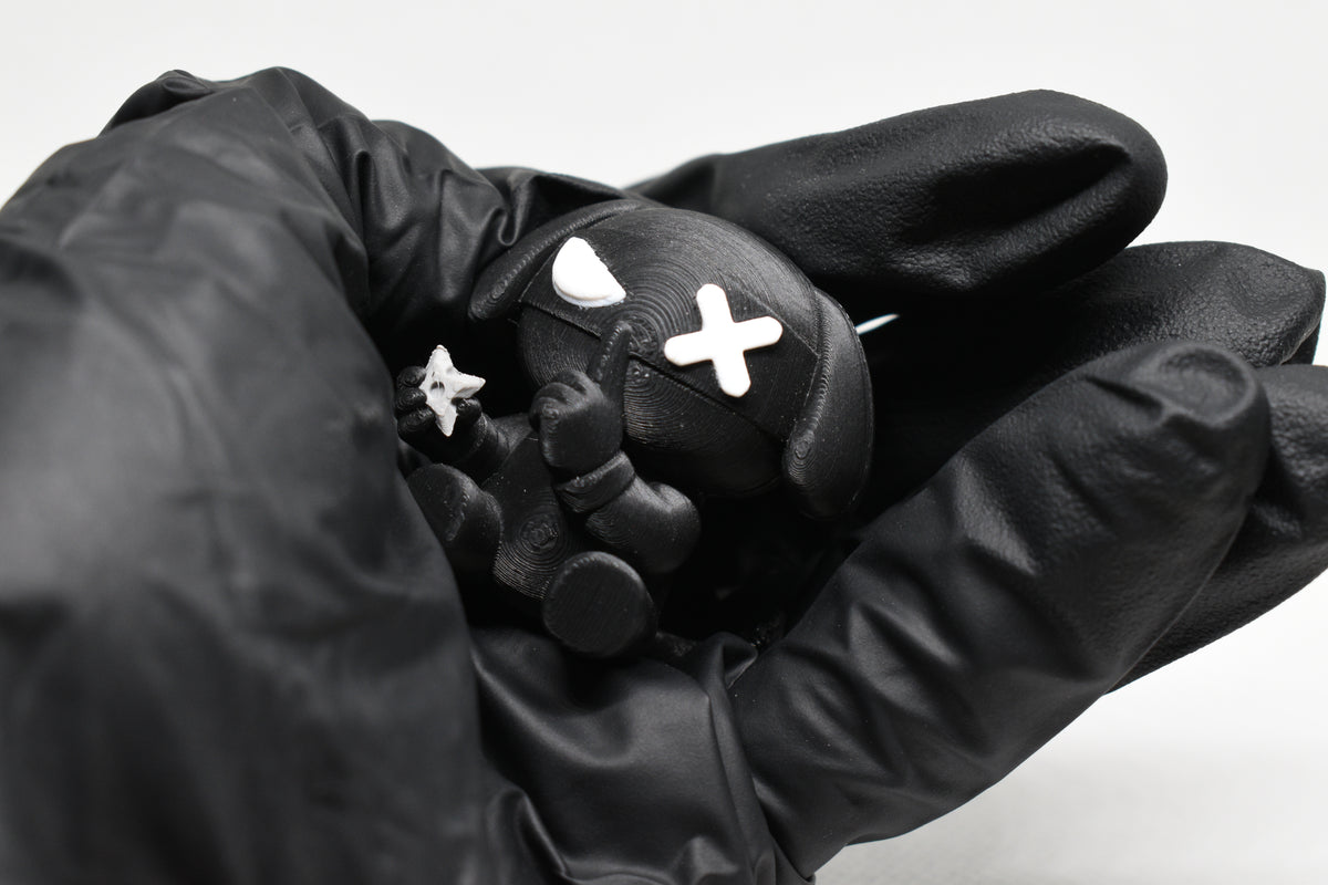 Hand in black glove holding 3D printed black monomoodz ninja glyphie dog figure holding a mini shuriken close up by LayerPlay