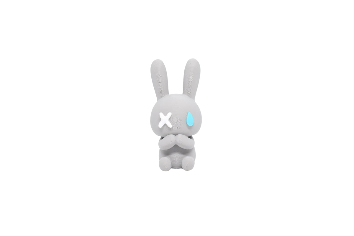 3D printed grey monomoodz nixie rabbit desk figure with white X eye, blue teardrop eye, and long bunny ears front view by LayerPlay
