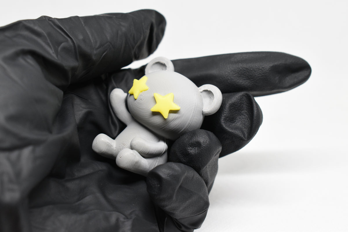 Hand in black glove holding cute 3D printed grey monomoodz twinkle bear desk figure close up by LayerPlay