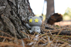 3D printed grey monomoodz twinkle desk figure sitting outdoors against a tree trunk on pine needles by LayerPlay