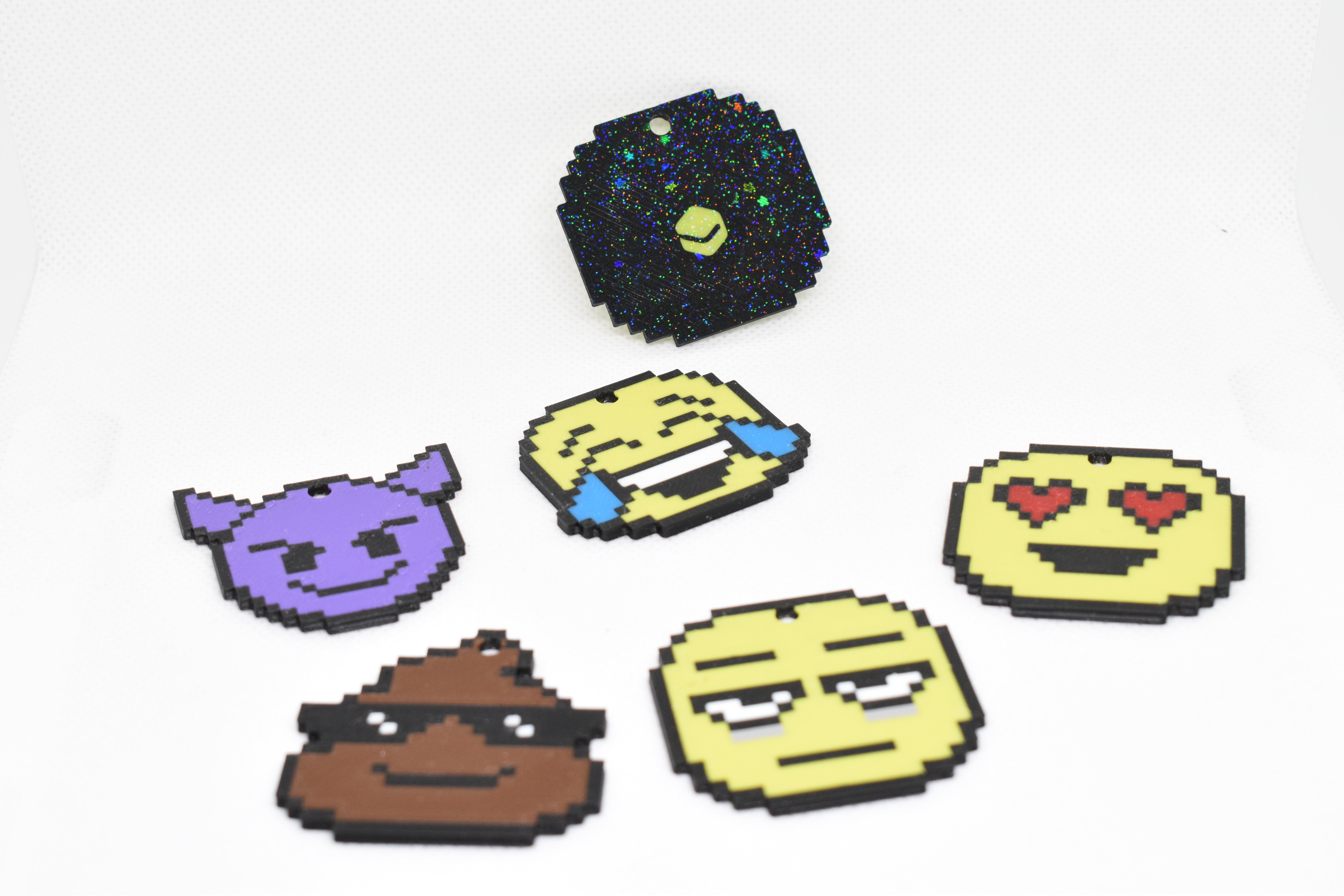 Pixelated emoji keychains arranged on a white background, including devil, laughing, heart‑eyes, poop, and neutral faces.