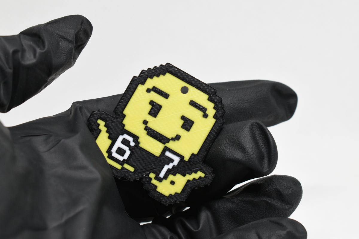 Hand in black glove holding 3D printed pixel 6 7 emoji keychain front view detail by LayerPlay
