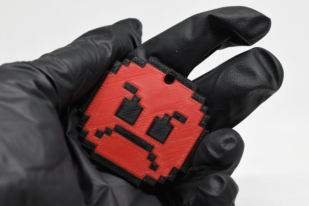 Hand in black glove holding 3D printed red pixel angry emoji keychain front view detail by LayerPlay