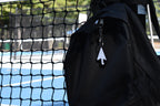 Pixelated arrow cursor keychain clipped to a black backpack zipper outdoors near a tennis court by LayerPlay