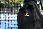 Ascended Duck pixel rubber duck keychain clipped to a black backpack zipper outdoors near a tennis court by LayerPlay
