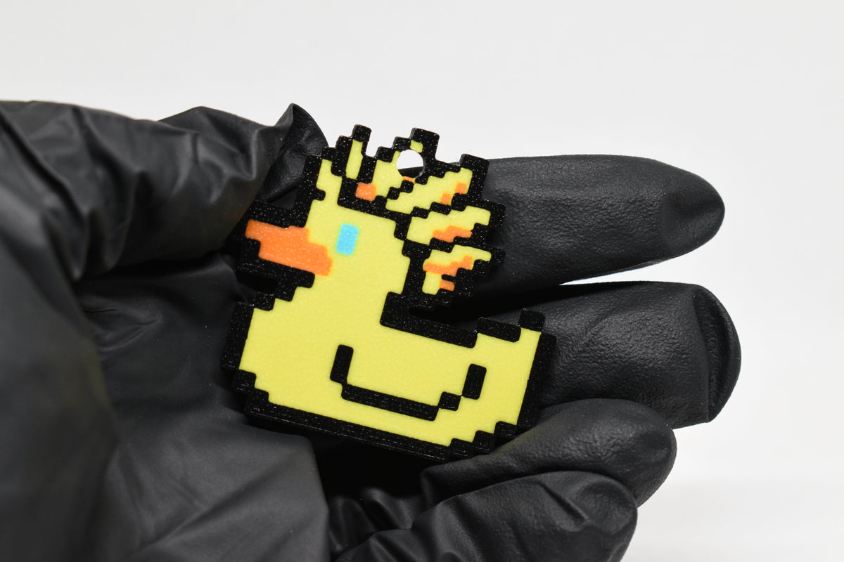 Hand in black glove holding 3D printed retro Ascended Duck pixel rubber duck keychain front view detail by LayerPlay