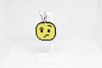 3D printed retro pixelated confused face emoji keychain hanging on a white display stand by LayerPlay