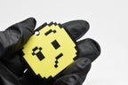 Hand in black glove holding 3D printed pixel confused face emoji keychain front view detail by LayerPlay