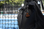 Pixelated cool poop emoji keychain clipped to a black backpack zipper outdoors near a tennis court by LayerPlay
