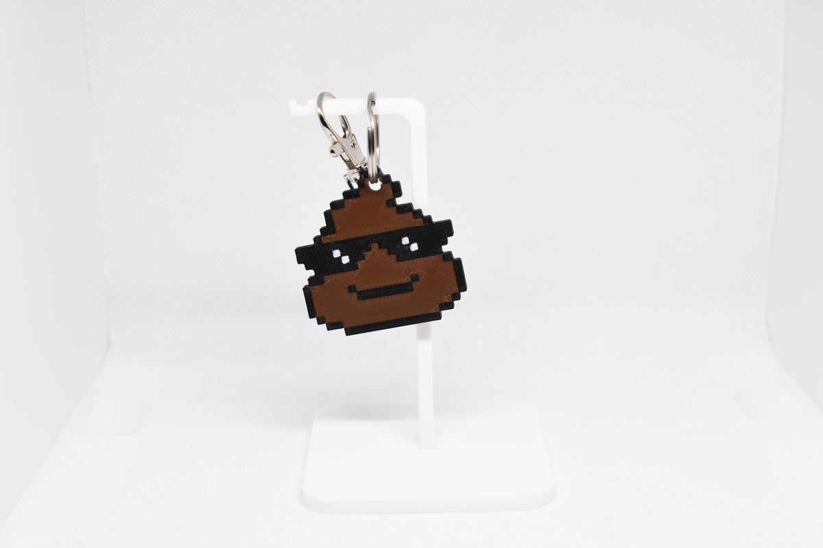 3D printed retro pixelated cool poop emoji keychain wearing sunglasses hanging on a white display stand by LayerPlay