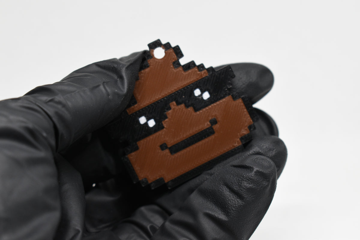 Hand in black glove holding 3D printed pixel cool poop emoji keychain wearing sunglasses front view detail by LayerPlay