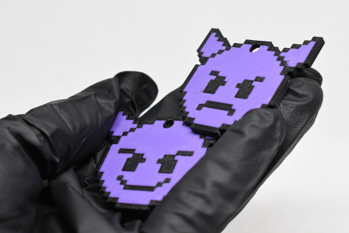 Hand in black glove holding 3D printed pixel devil emoji keychain front view detail by LayerPlay