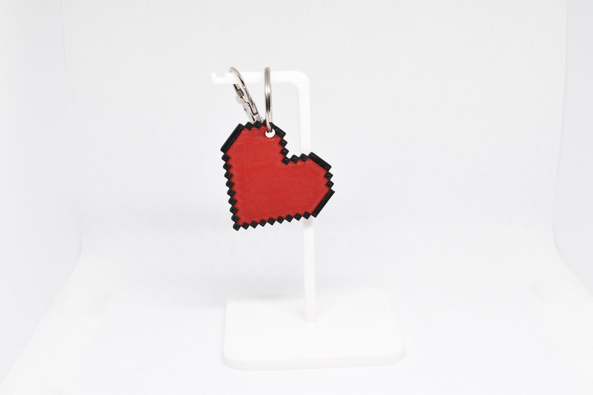 3D printed retro pixelated heart emoji keychain hanging on a white display stand by LayerPlay