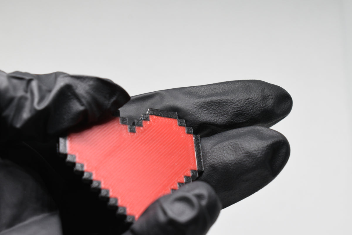Hand in black glove holding 3D printed pixel heart emoji keychain front view detail by LayerPlay