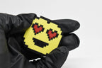 Hand in black glove holding 3D printed pixel heart eyes emoji keychain front view detail by LayerPlay