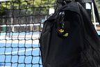 Hoodie Duck pixel rubber duck keychain clipped to a black backpack zipper outdoors near a tennis court by LayerPlay