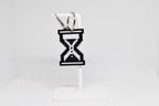 3D printed pixelated hourglass cursor keychain hanging on a white display stand by LayerPlay
