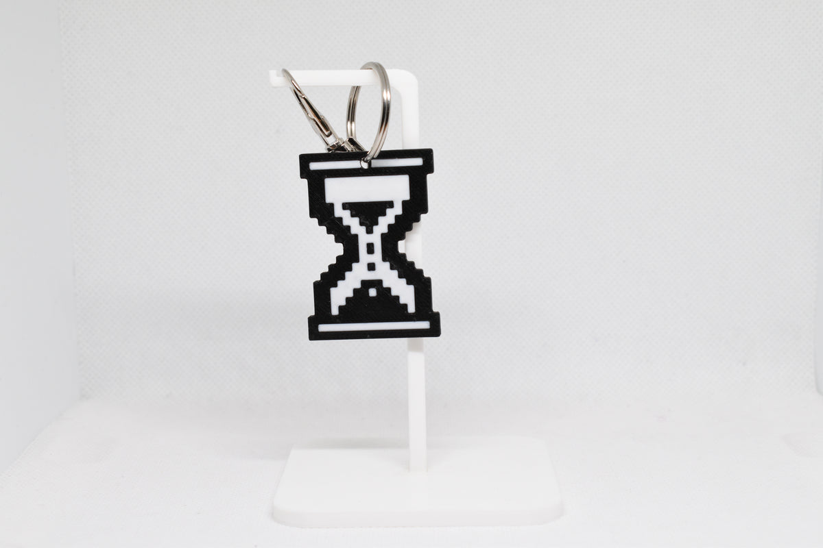 3D printed pixelated hourglass cursor keychain hanging on a white display stand by LayerPlay