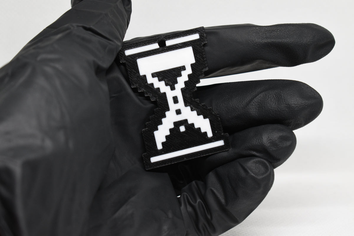 Hand in black glove holding 3D printed retro pixel hourglass cursor keychain front view detail by LayerPlay
