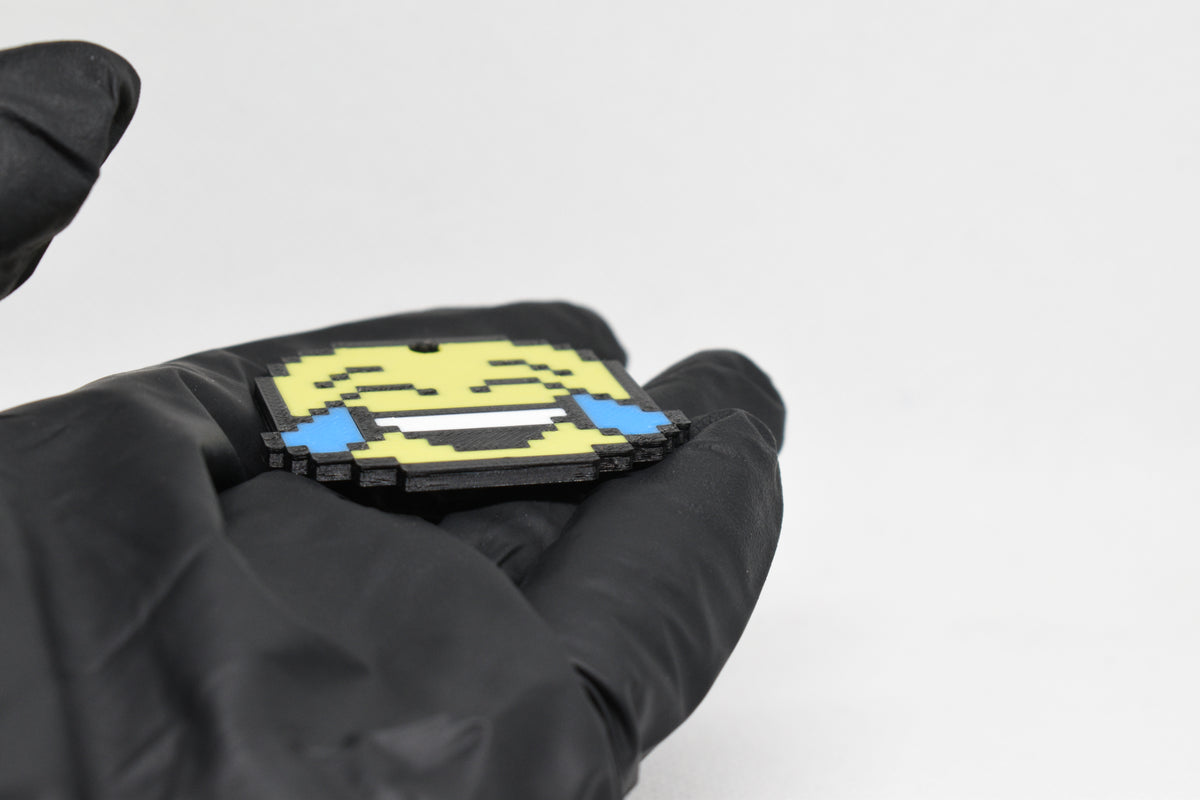 Side angle view showing 3D layered pixel detail and thickness of pixelated laughing emoji keychain by LayerPlay