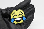 Hand in black glove holding 3D printed pixel laughing face emoji keychain front view detail by LayerPlay