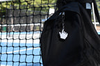 Pixelated pointing hand cursor keychain clipped to a black backpack zipper outdoors near a tennis court by LayerPlay