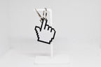 3D printed pixelated pointing hand pointer cursor keychain hanging on a white display stand by LayerPlay