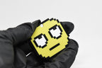 Hand in black glove holding 3D printed pixel rolling eyes emoji keychain front view detail by LayerPlay