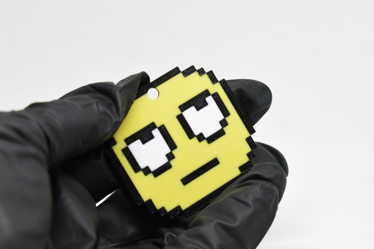 Hand in black glove holding 3D printed pixel rolling eyes emoji keychain front view detail by LayerPlay