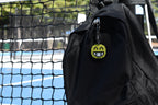 Pixelated smiling face emoji keychain clipped to a black backpack zipper outdoors near a tennis court by LayerPlay
