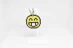 3D printed retro pixelated smiling face emoji keychain hanging on a white display stand by LayerPlay