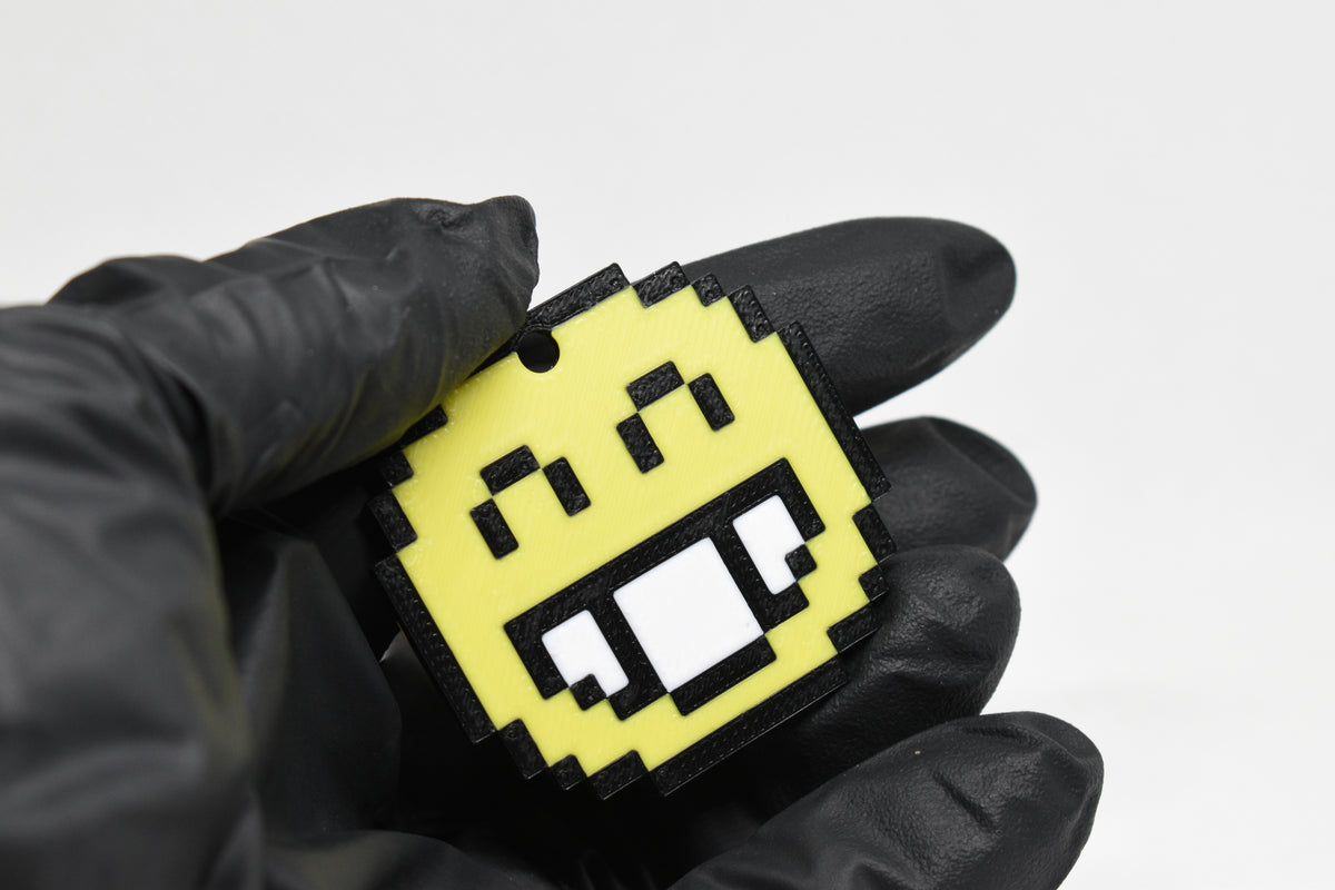 Hand in black glove holding 3D printed pixel smiling face emoji keychain front view detail by LayerPlay