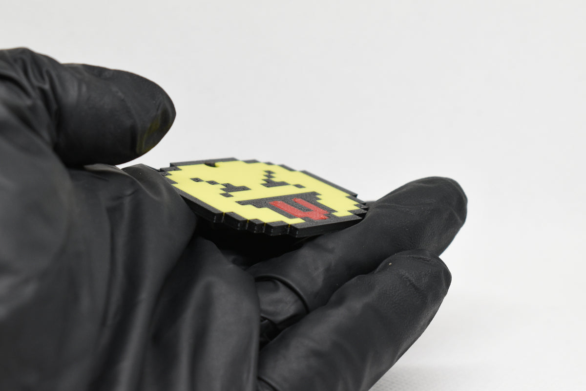 Side angle view showing 3D layered pixel detail and thickness of pixelated squinting face emoji keychain by LayerPlay