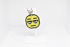 3D printed retro pixelated tired face emoji keychain hanging on a white display stand by LayerPlay