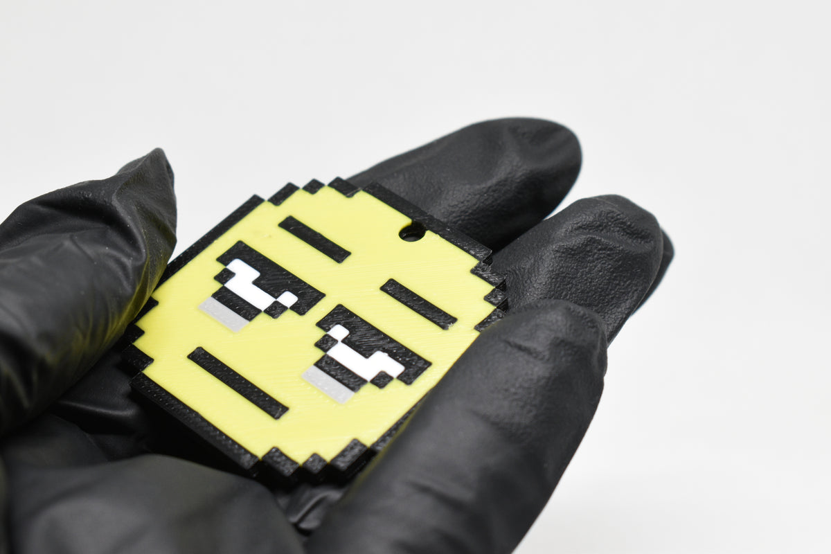 Hand in black glove holding 3D printed pixel tired emoji keychain front view detail by LayerPlay