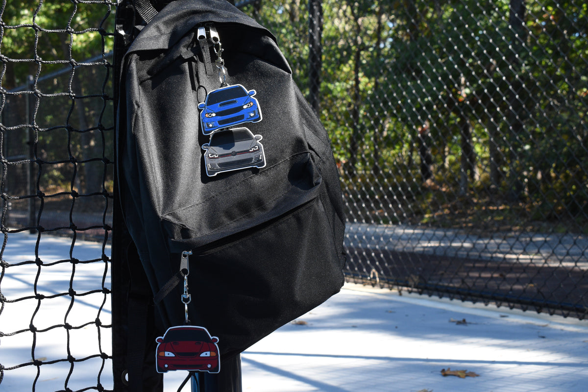 3D printed Pocket Motors mini car keychains clipped onto a black canvas backpack hanging outdoors by LayerPlay