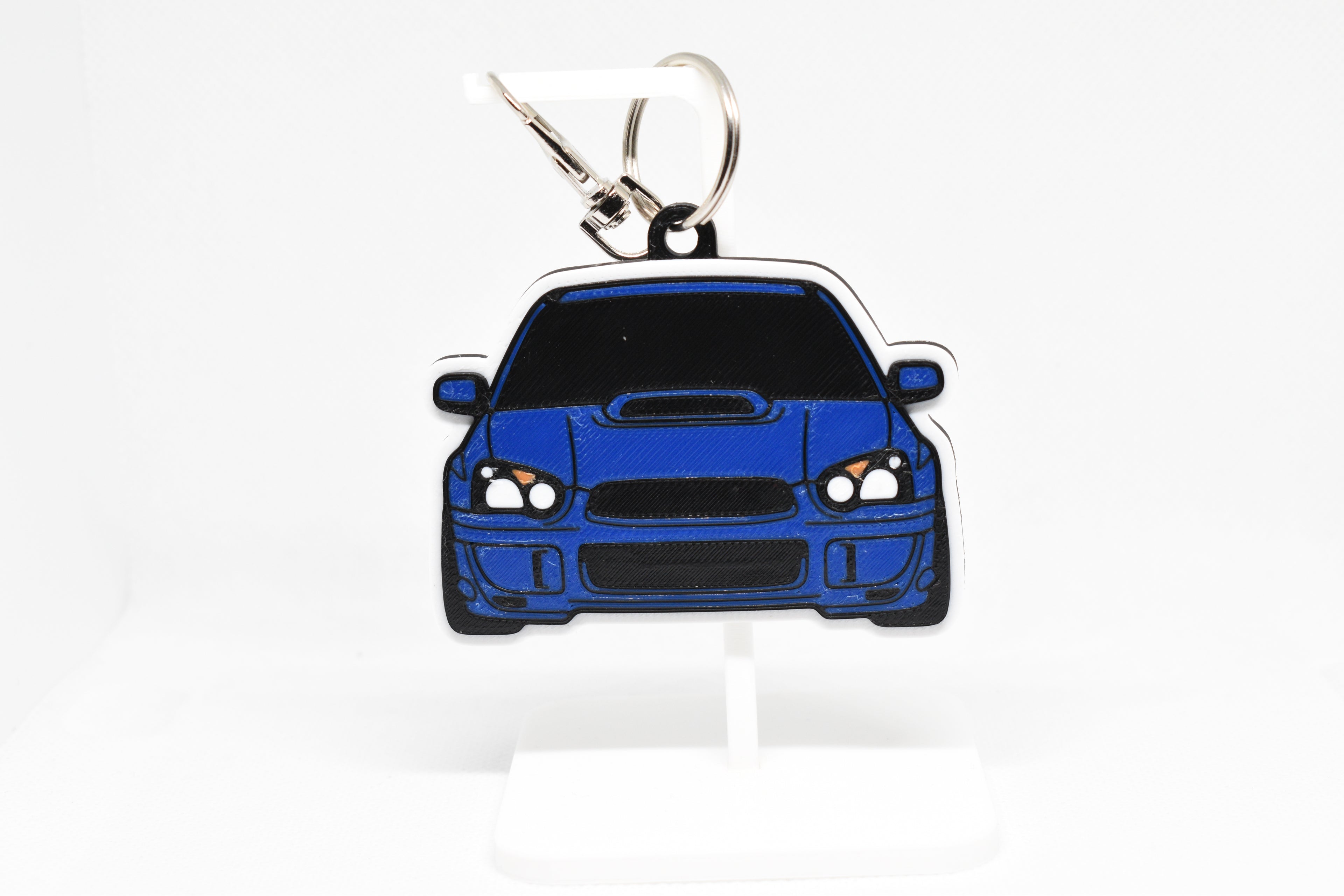 Pocket Motors Blobeye WRX STI keychain displayed on a white stand with metal ring and clip.
