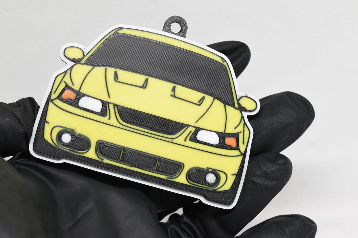 3D printed yellow Ford Mustang Cobra SN95 facelift keychain held in hand, front view detail by LayerPlay Pocket Motors