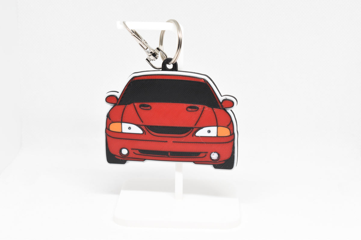 Pocket Motors Ford Mustang Cobra SN95 keychain displayed on a white stand with metal ring and clip.
