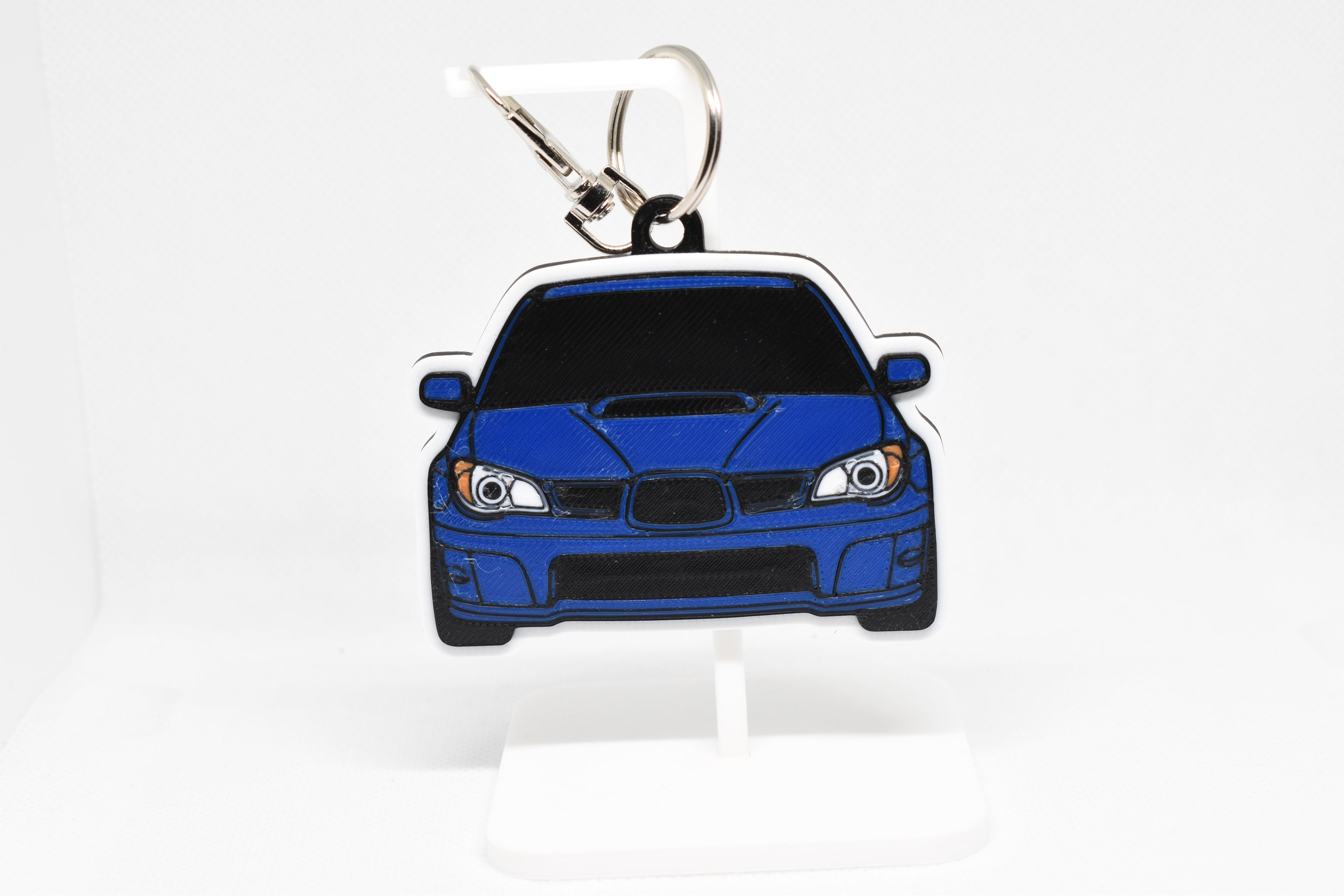 Pocket Motors Hawkeye WRX STI keychain displayed on a white stand with metal ring and clip.